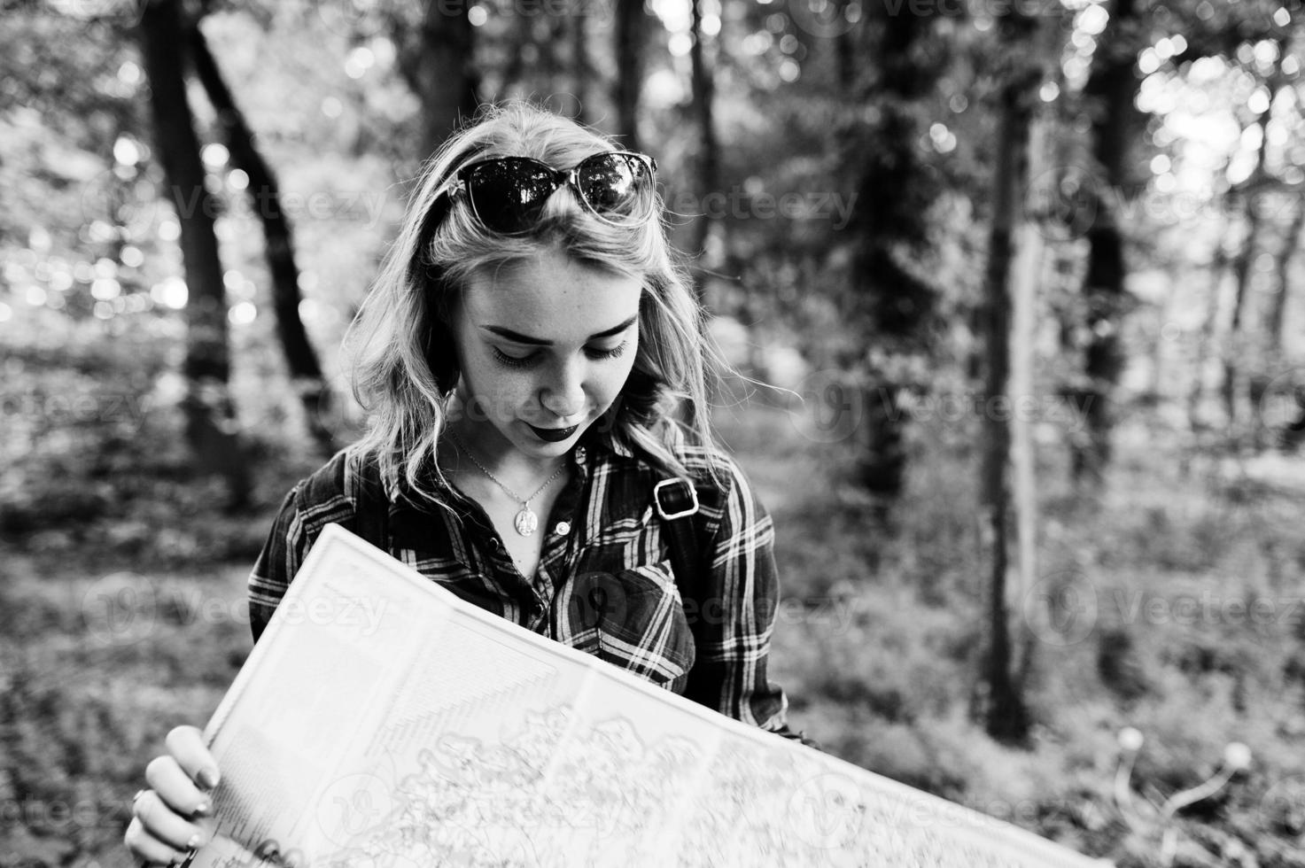 retrato de uma jovem linda loira de camisa xadrez segurando um mapa na floresta. foto