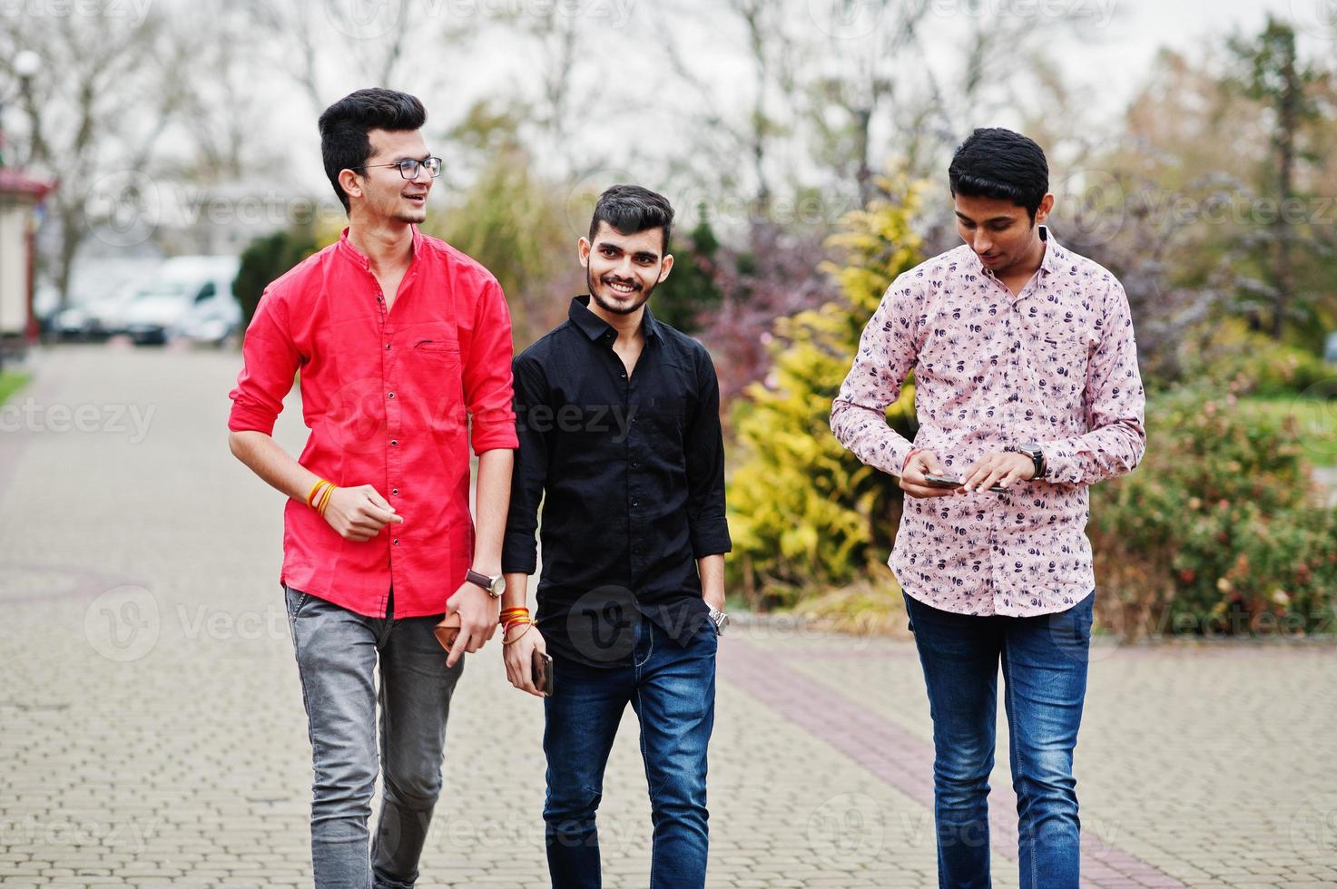 três caras indianos estudantes amigos andando na rua e olhando para o celular. foto