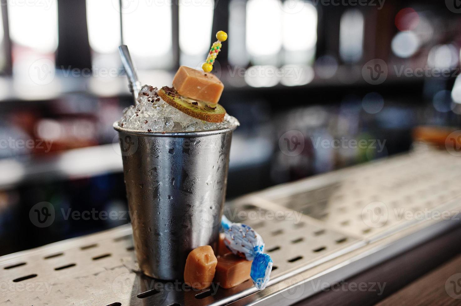 coquetel alcoólico com doces e balas em pequeno balde de prata na mesa do bar. foto