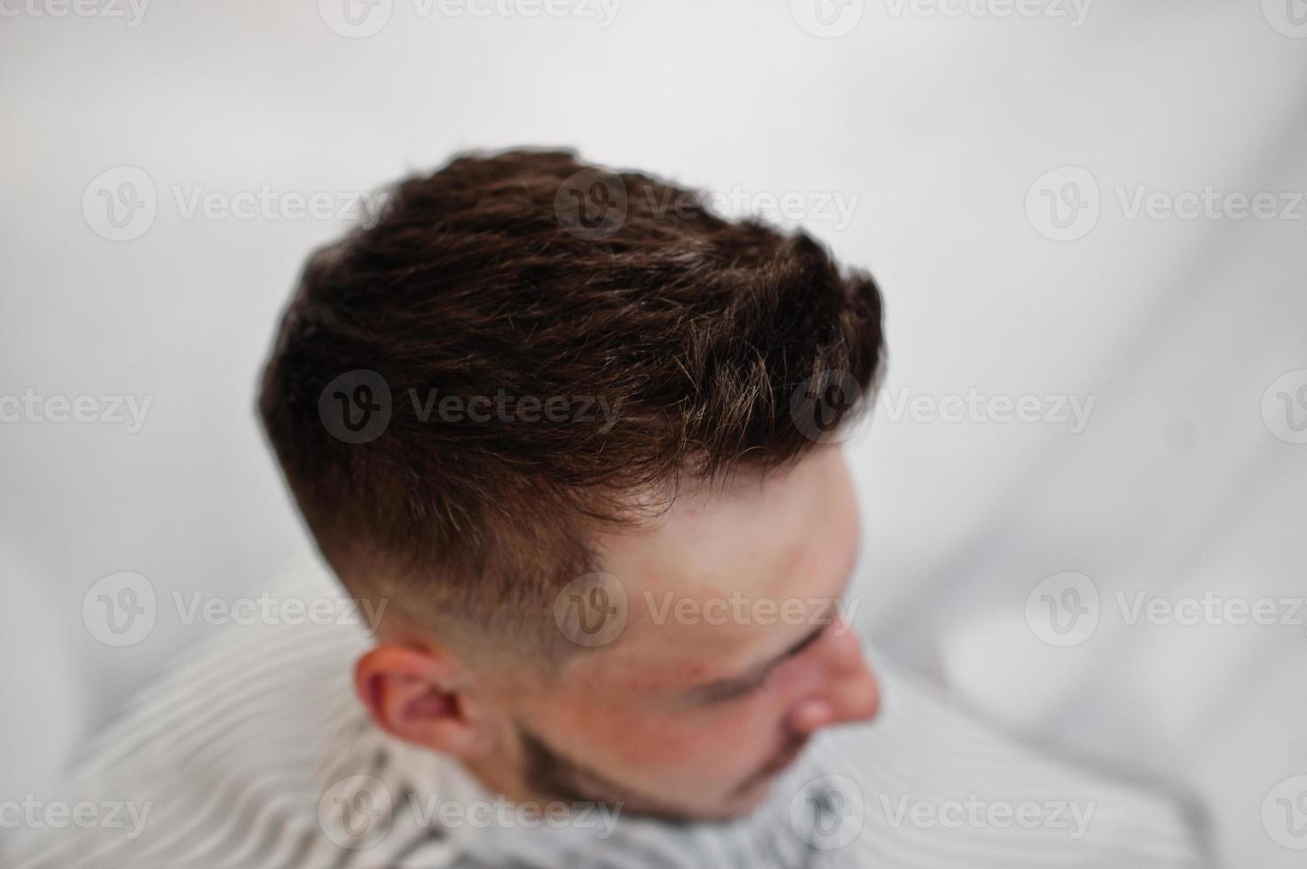 feche a cabeça do jovem barbudo cortando o cabelo na barbearia. alma de barbeiro. foto