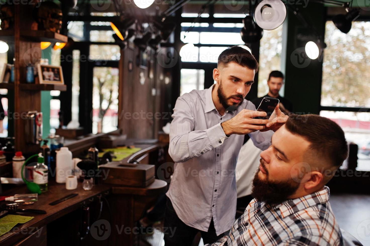 homem barbudo bonito na barbearia, barbeiro no trabalho, fazendo foto em seu telefone.
