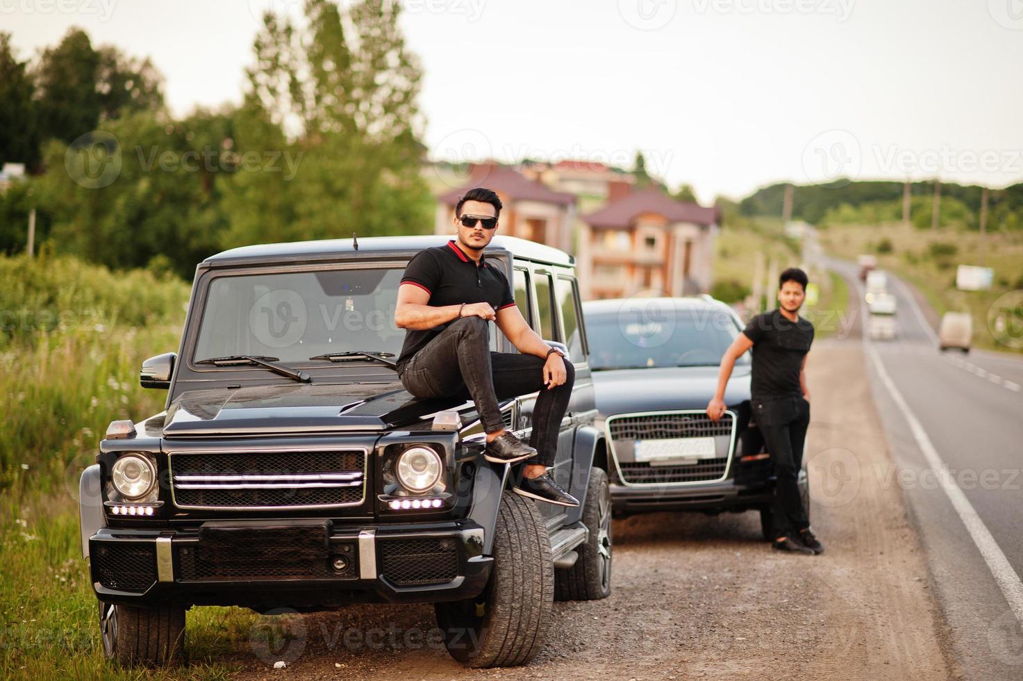 dois irmãos asiáticos vestem todo preto posando perto de carros suv. foto