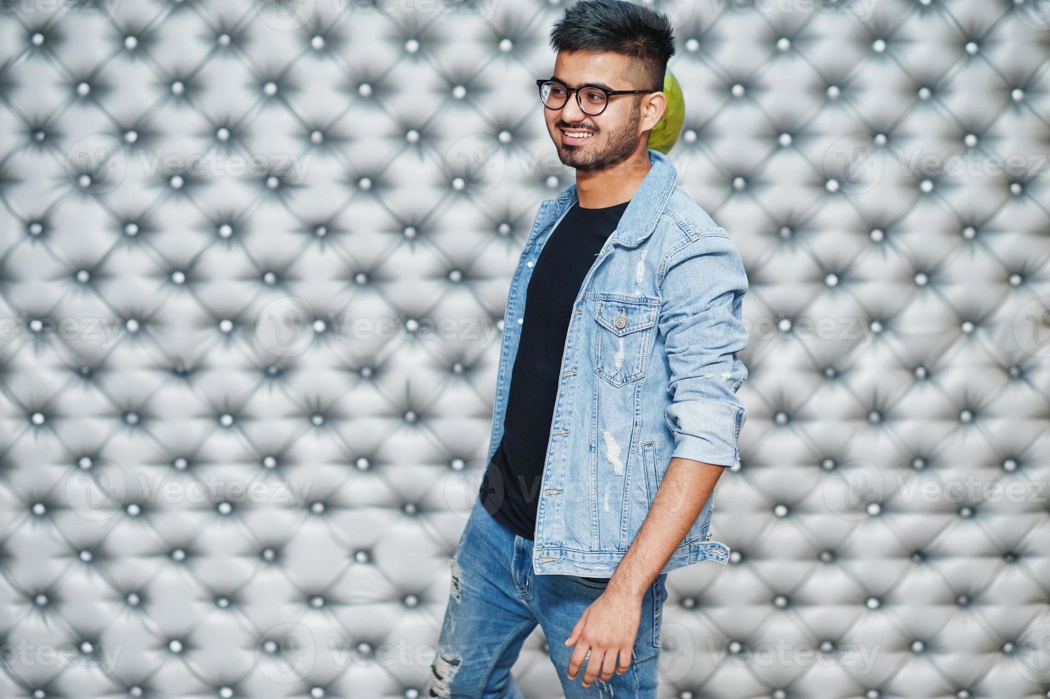 elegante homem asiático de jaqueta jeans e óculos com bola de boliche na mão contra o fundo da parede prata. foto