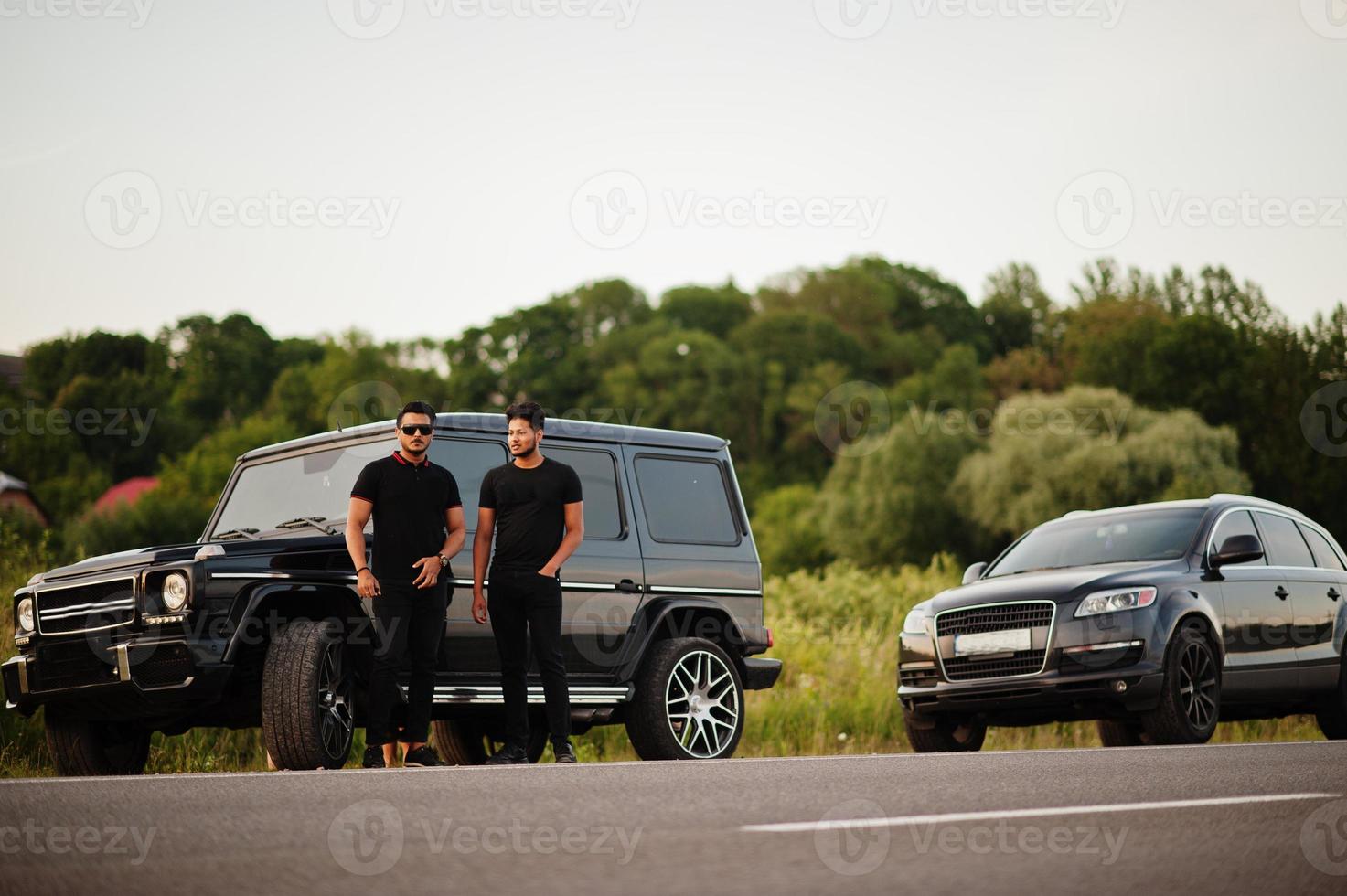 dois irmãos asiáticos vestem todo preto posando perto de carros suv. foto