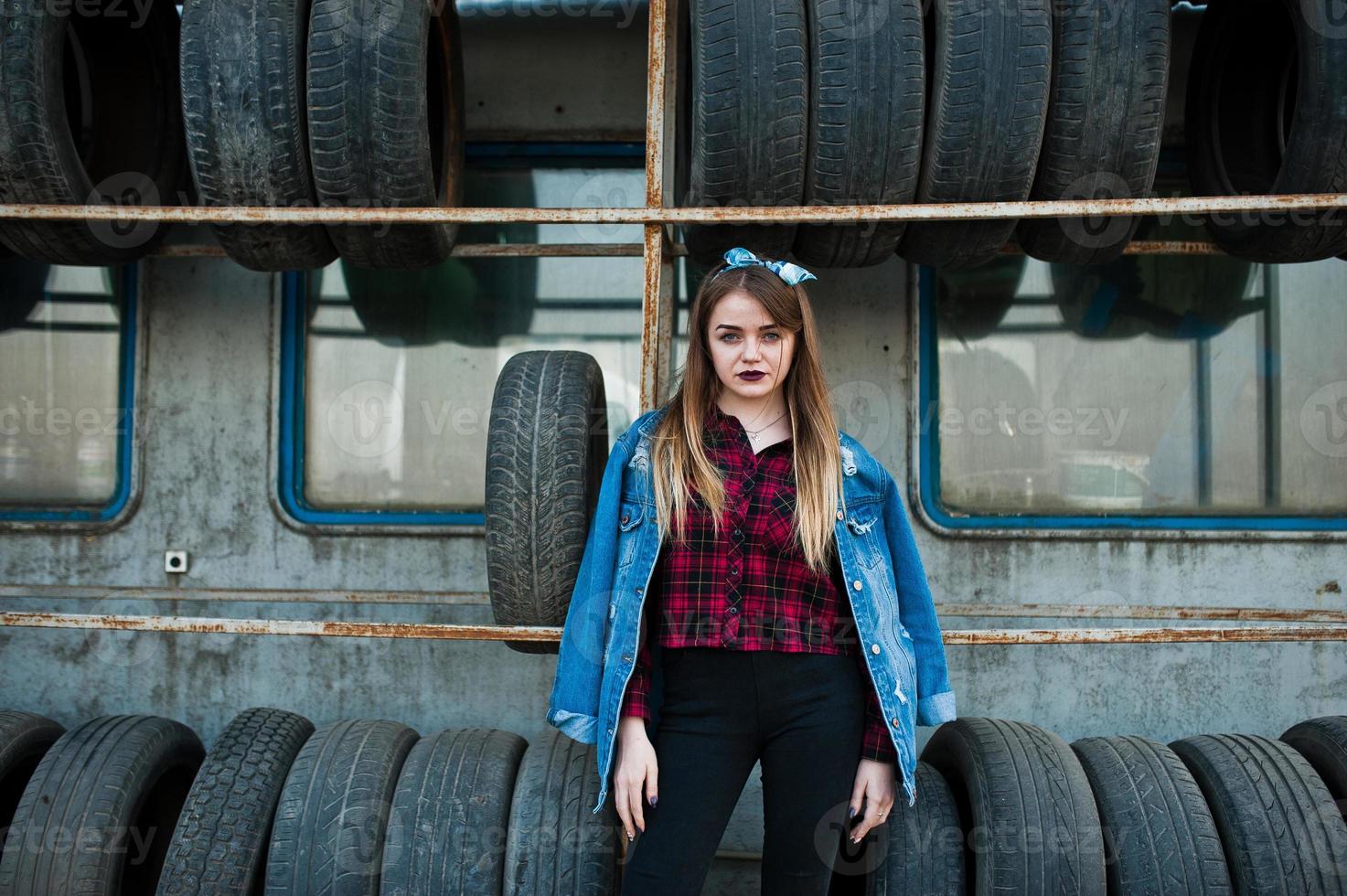 garota jovem hippie na jaqueta jeans e lenço na cabeça na zona de montagem do pneu. foto