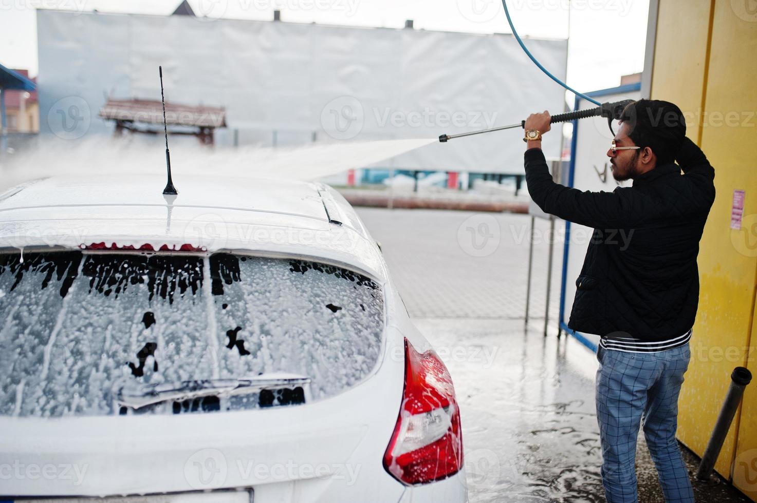 homem do sul da Ásia ou homem indiano lavando seu transporte branco na lavagem de carros. foto