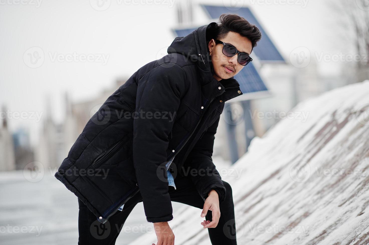 casual jovem indiano na jaqueta preta e óculos de sol posou no dia de inverno. foto