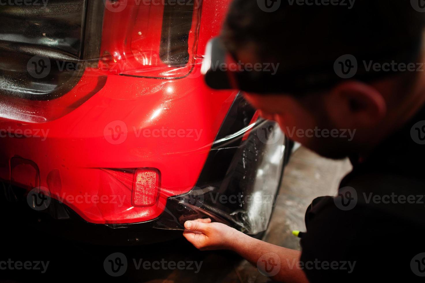 trabalhador de serviço de carro colocou filme anti cascalho em um corpo de carro vermelho na oficina de detalhamento de veículos. proteção do carro com películas especiais. foto