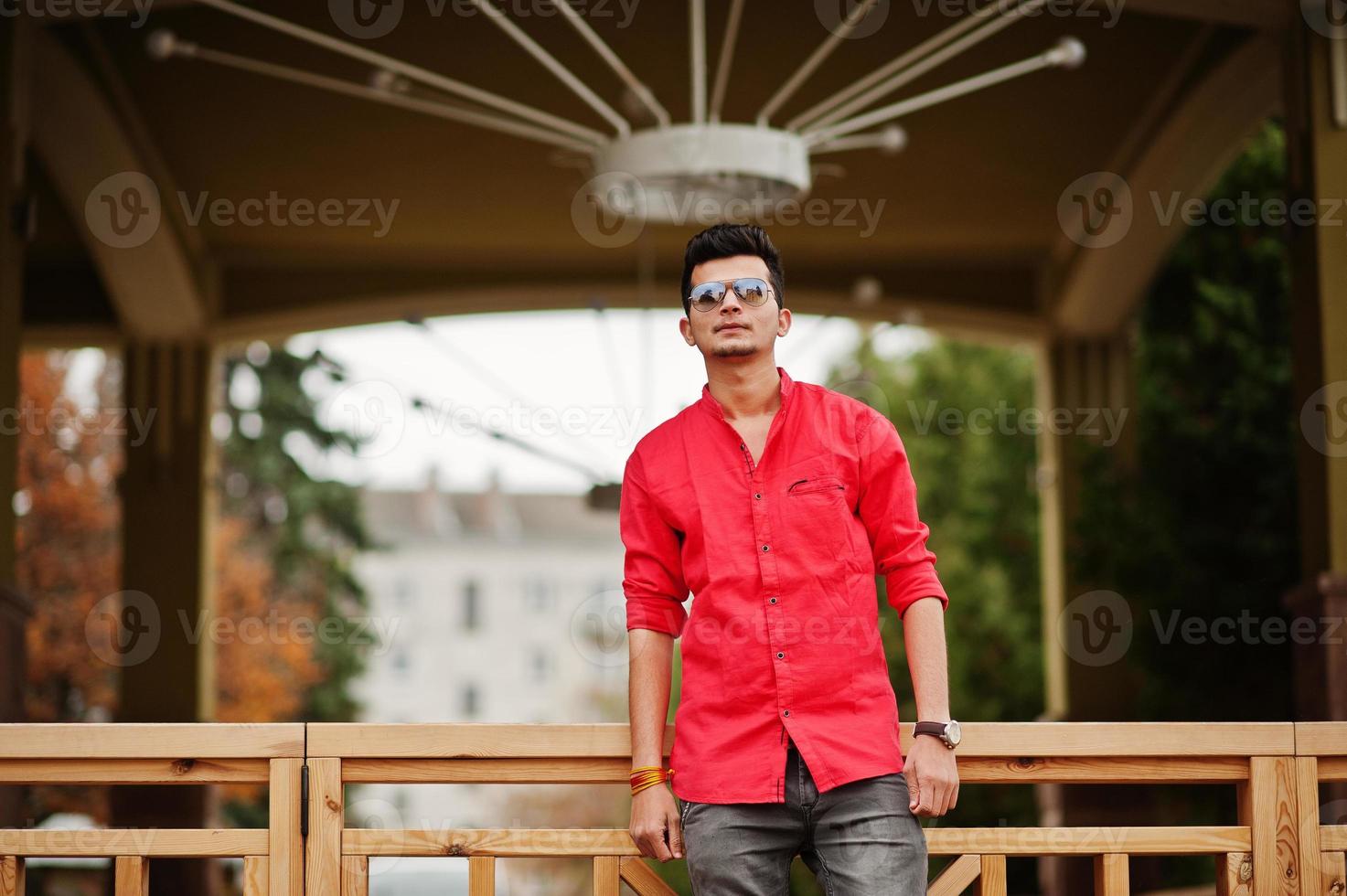 homem indiano de camisa vermelha e óculos de sol posou ao ar livre. foto