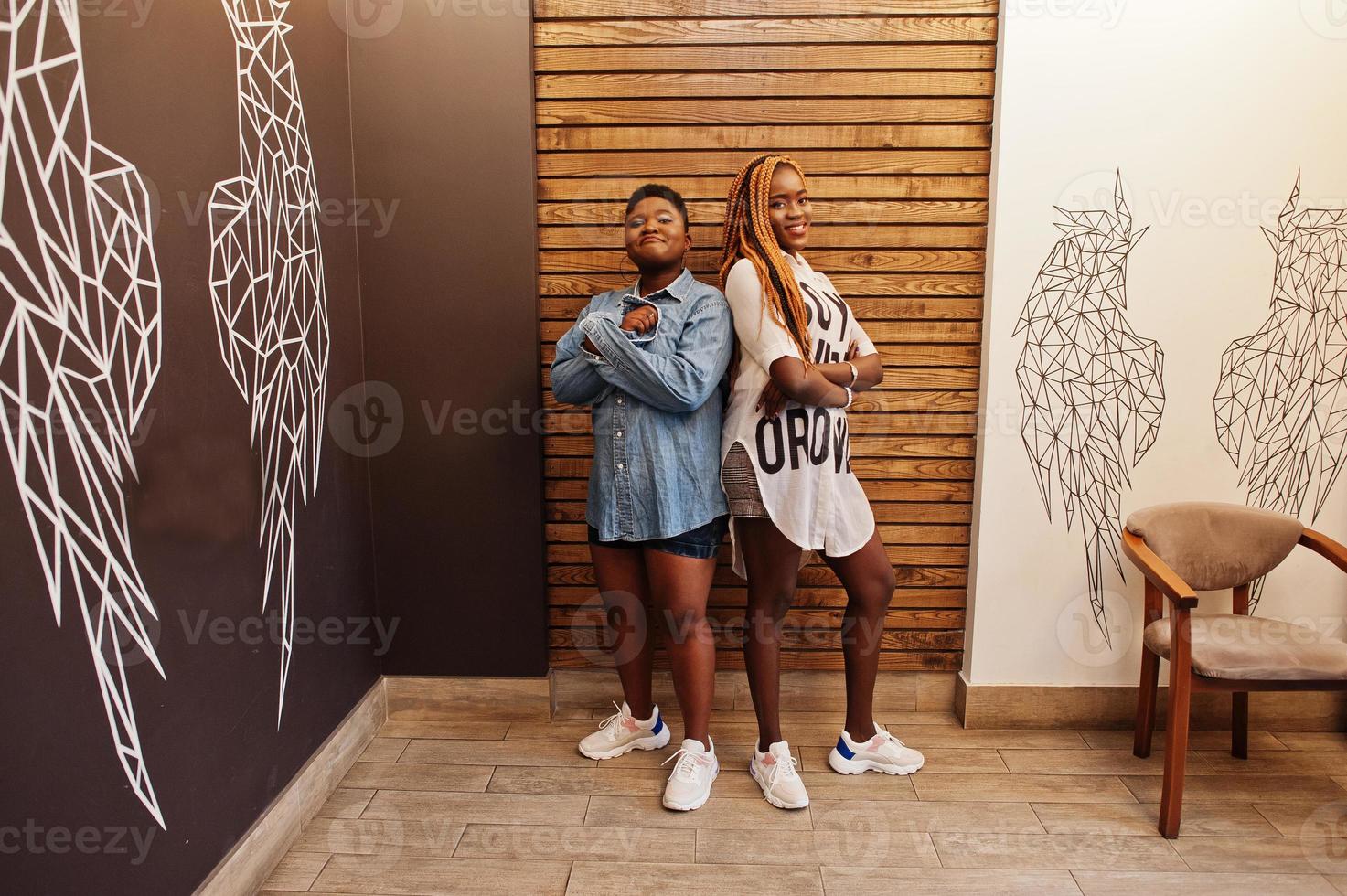 duas mulheres africanas em roupas casuais elegantes posando contra a parede de asas de anjo. foto