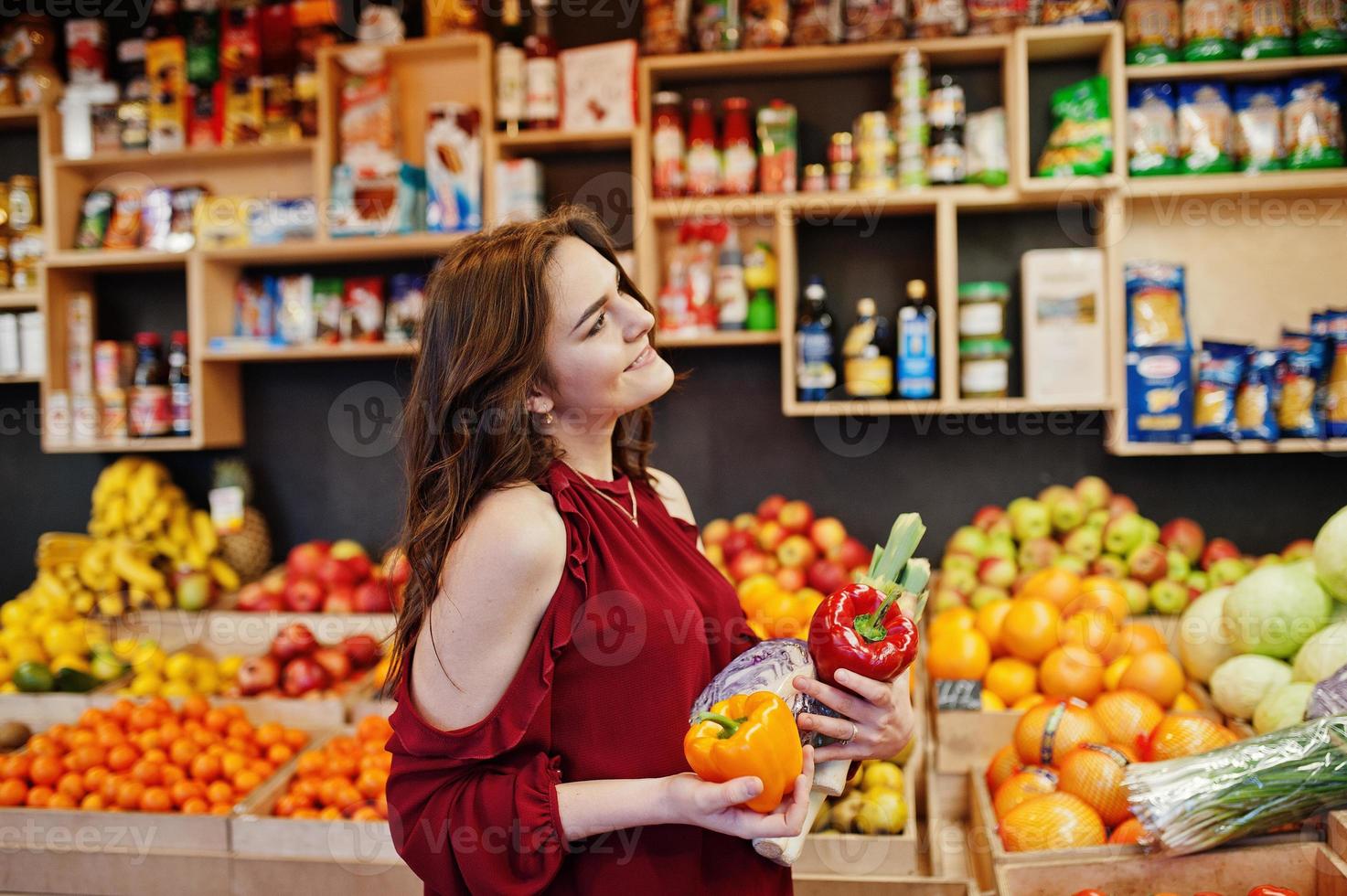 garota de vermelho segurando diferentes vegetais na loja de frutas. foto