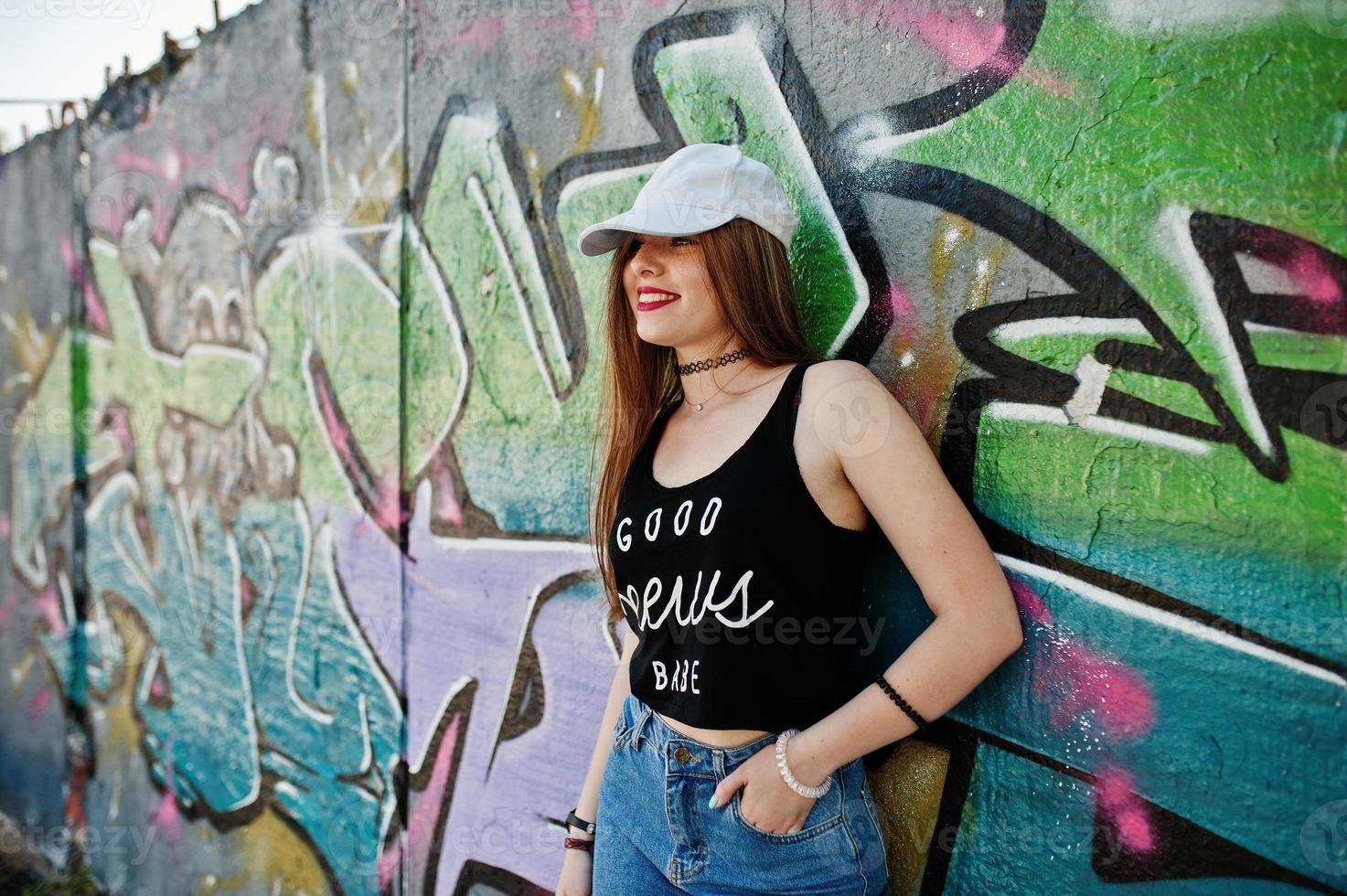 garota elegante hipster casual em boné e jeans usam contra parede de graffiti grande. foto