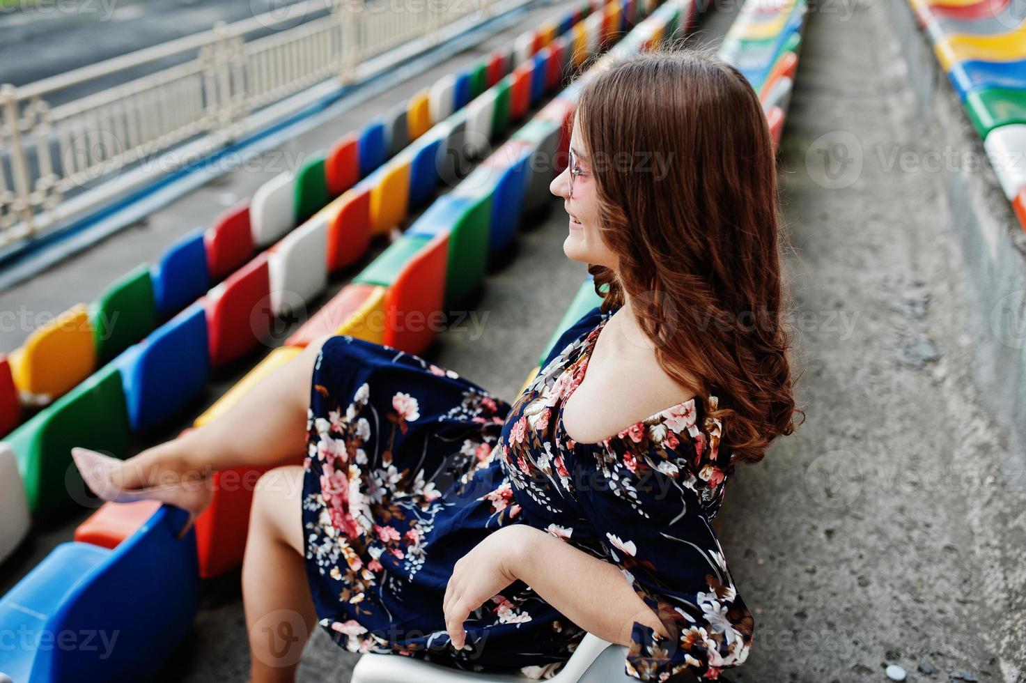 retrato de uma jovem linda de vestido e óculos de sol, sentado nas tribunas no estádio. foto