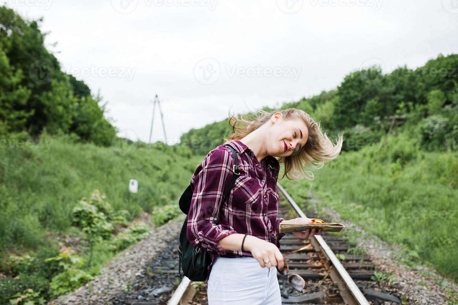 retrato de uma menina bonita loira na camisa tartan andando na ferrovia com mapa nas mãos dela. foto