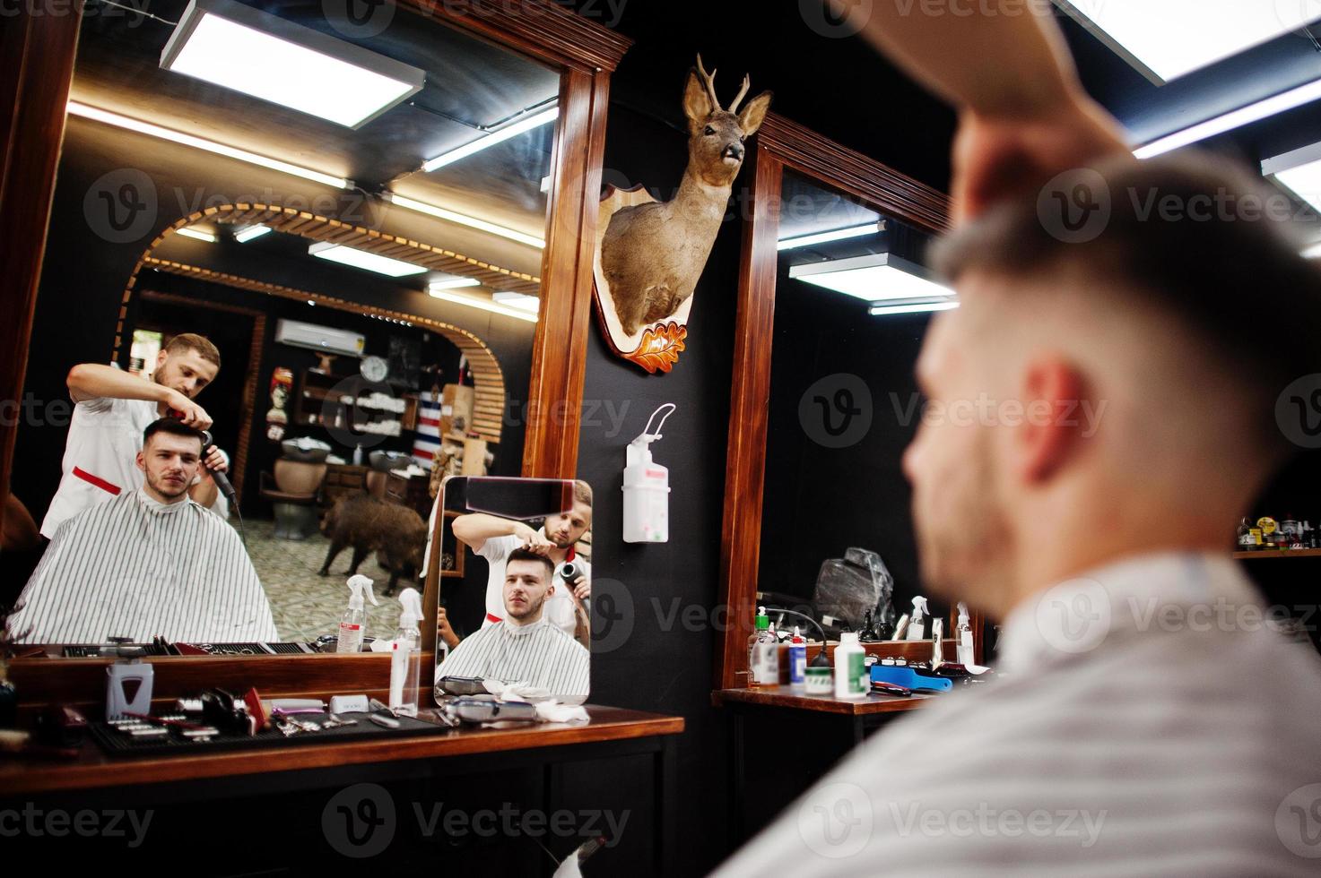 jovem barbudo cortando o cabelo pelo cabeleireiro enquanto está sentado na cadeira na barbearia. alma de barbeiro. foto