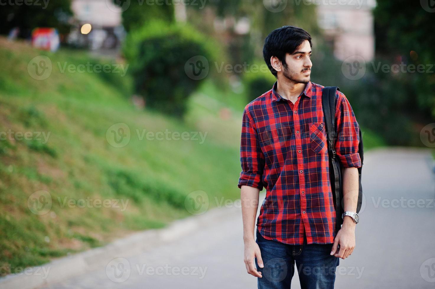 homem jovem estudante indiano na camisa xadrez vermelha e jeans com mochila posou na rua. foto