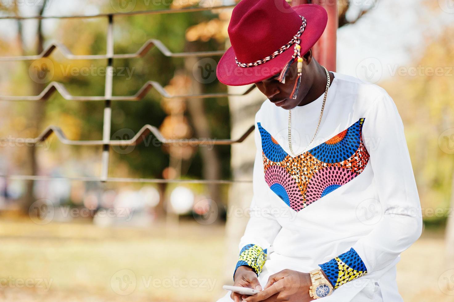 homem elegante na moda afro frança de chapéu vermelho e roupa branca posou no dia de outono. cara de negócios modelo africano negro com telefone celular nas mãos. foto
