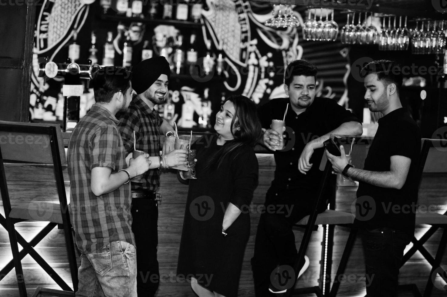 grupo de amigos indianos se divertindo e descansando na boate, bebendo coquetéis perto do balcão do bar. foto