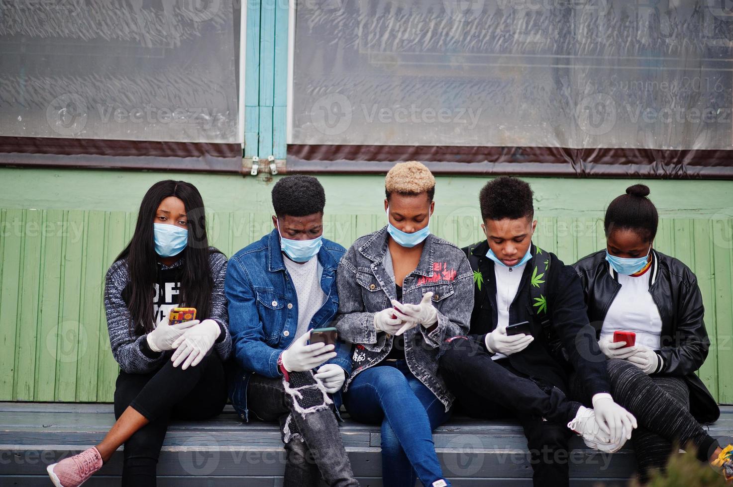 grupo de amigos adolescentes africanos sentados com telefones, usando máscaras médicas protegem contra infecções e doenças quarentena do vírus coronavírus. foto