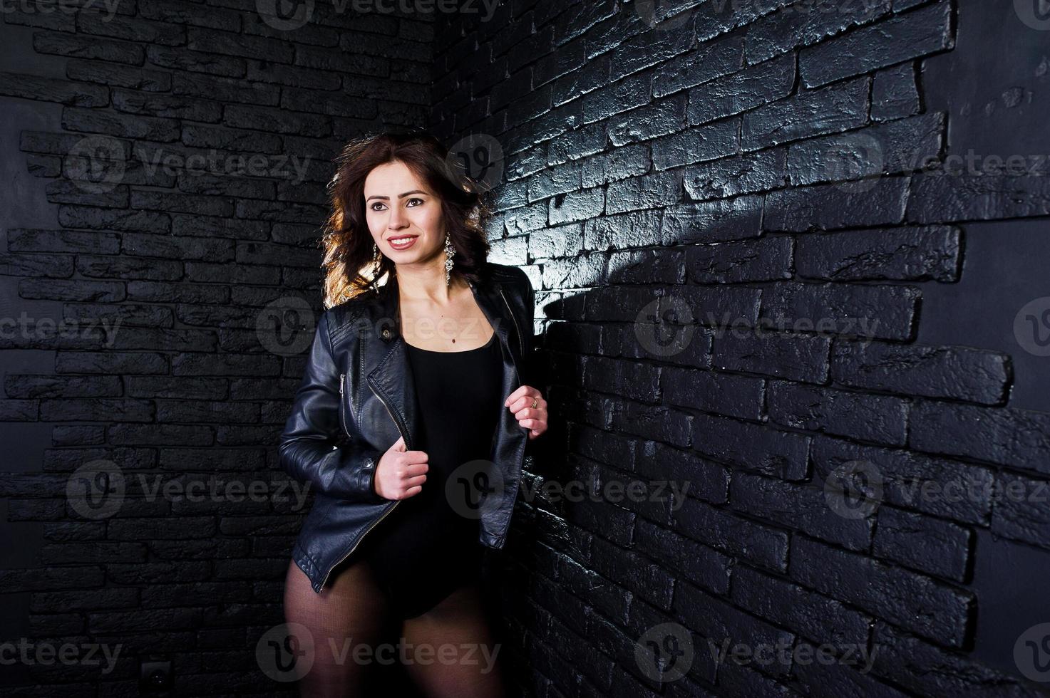 retrato de estúdio de menina morena sexy jaqueta de couro preta contra a parede de tijolos. foto