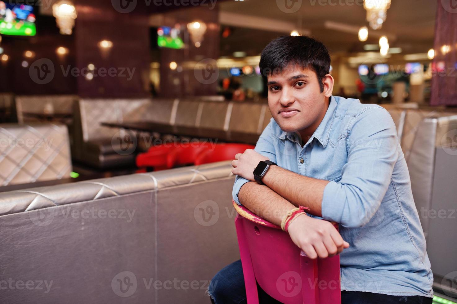 elegante homem asiático usar camisa jeans, sentado na cadeira contra bar no clube. foto