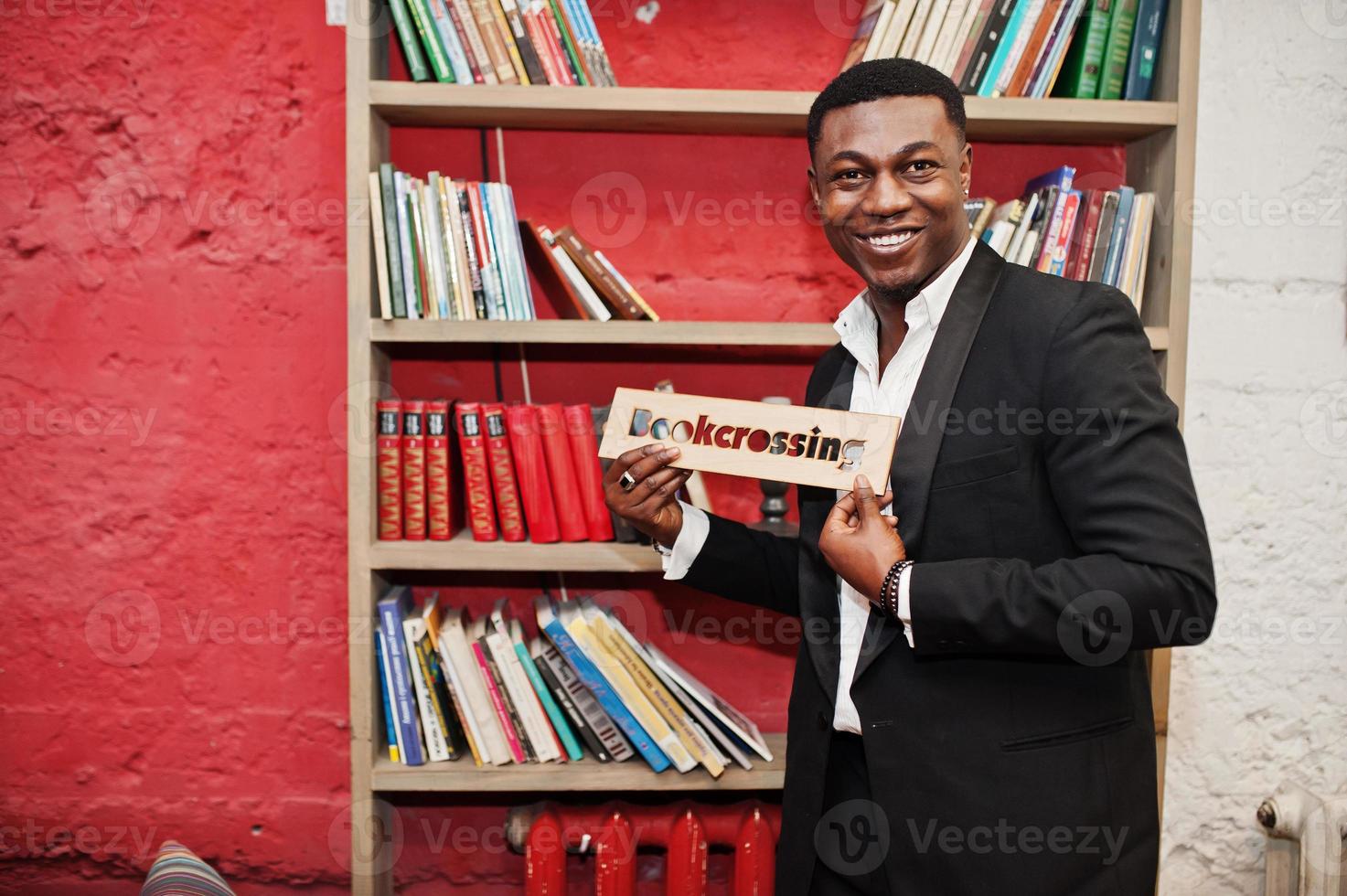 forte e poderoso homem afro-americano de terno preto contra prateleiras de livros em livros grátis anti café. foto