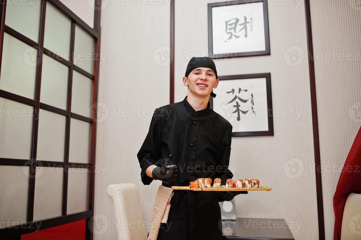 chef profissional veste de preto com sushi e pãezinhos em um restaurante de comida tradicional japonesa. foto