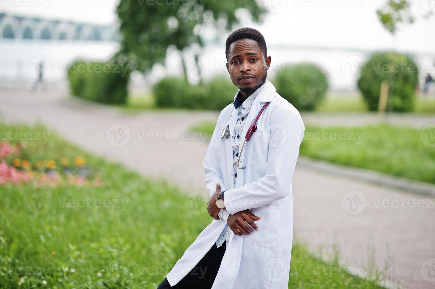 jovem médico americano africano de jaleco branco com um estetoscópio posado ao ar livre. foto