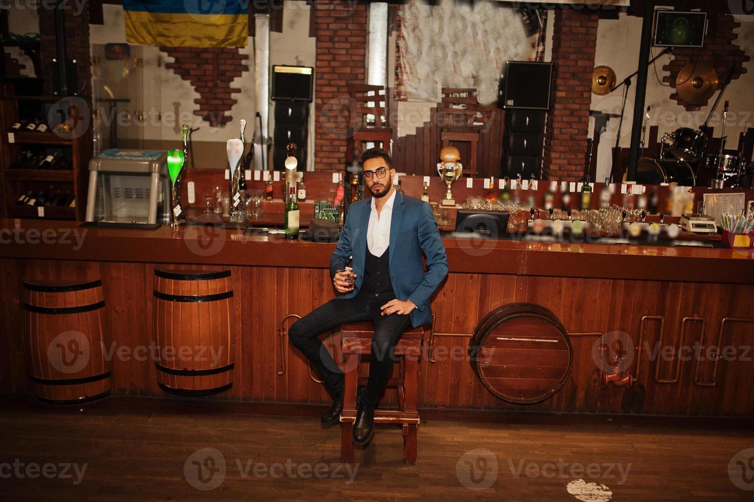 homem árabe bem vestido bonito com copo de uísque e charuto posou no pub. foto