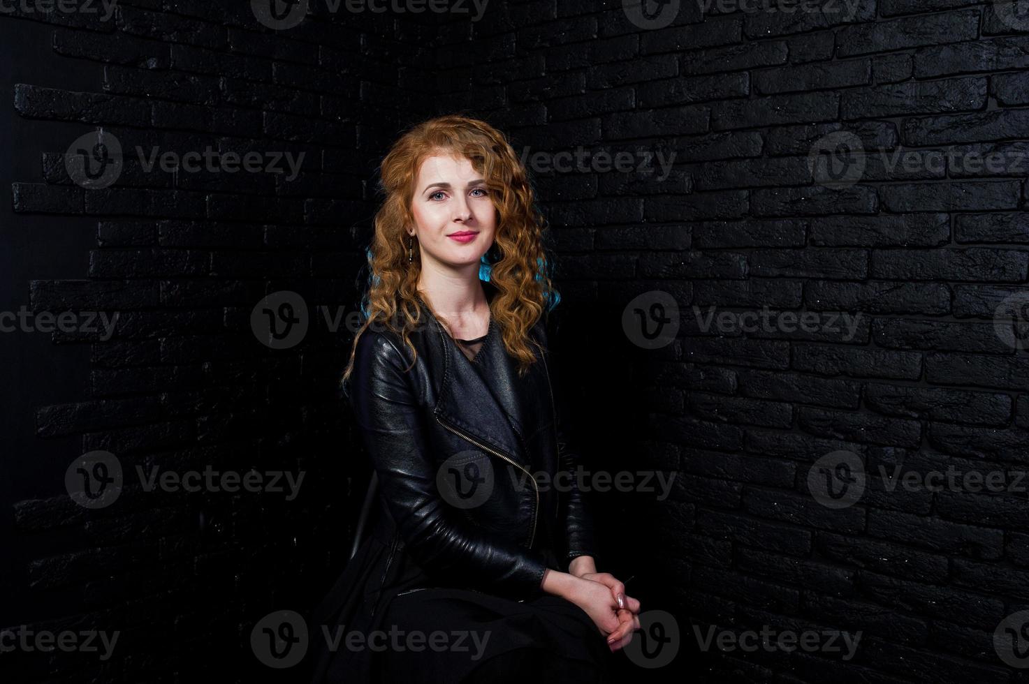 garota de cabelo encaracolado na jaqueta de couro no estúdio contra a parede de tijolo preto. foto
