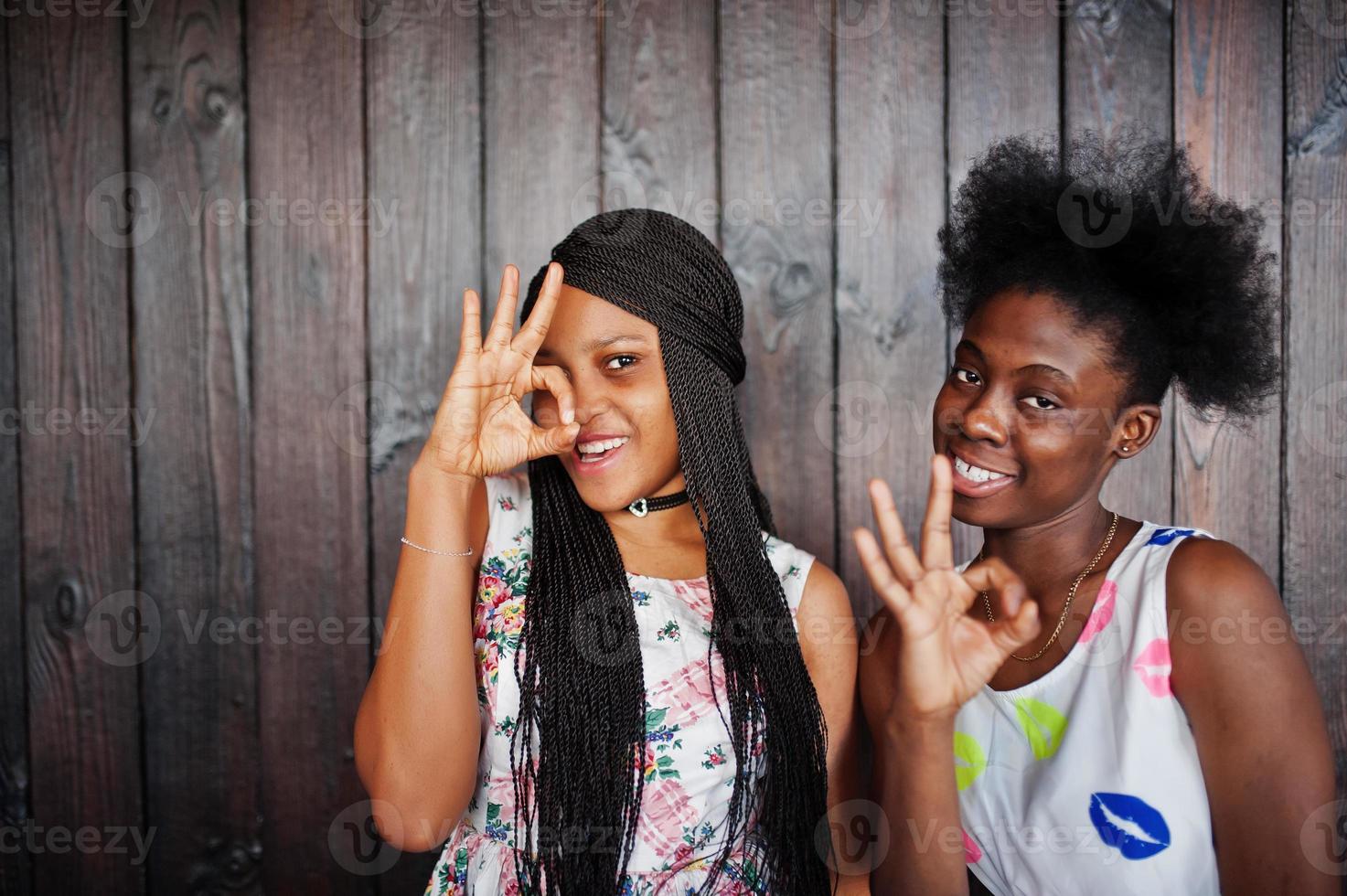 duas namoradas africanas negras em vestidos de verão posaram contra um fundo escuro de madeira e mostrando sinal de dedos bem. foto