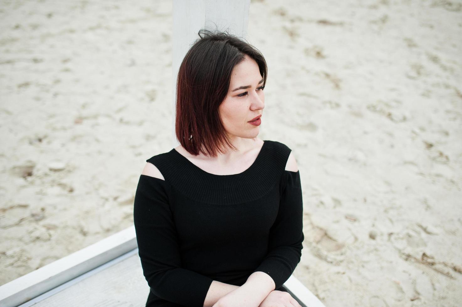 retrato de menina morena de vestido preto, sentado na construção de madeira branca. foto