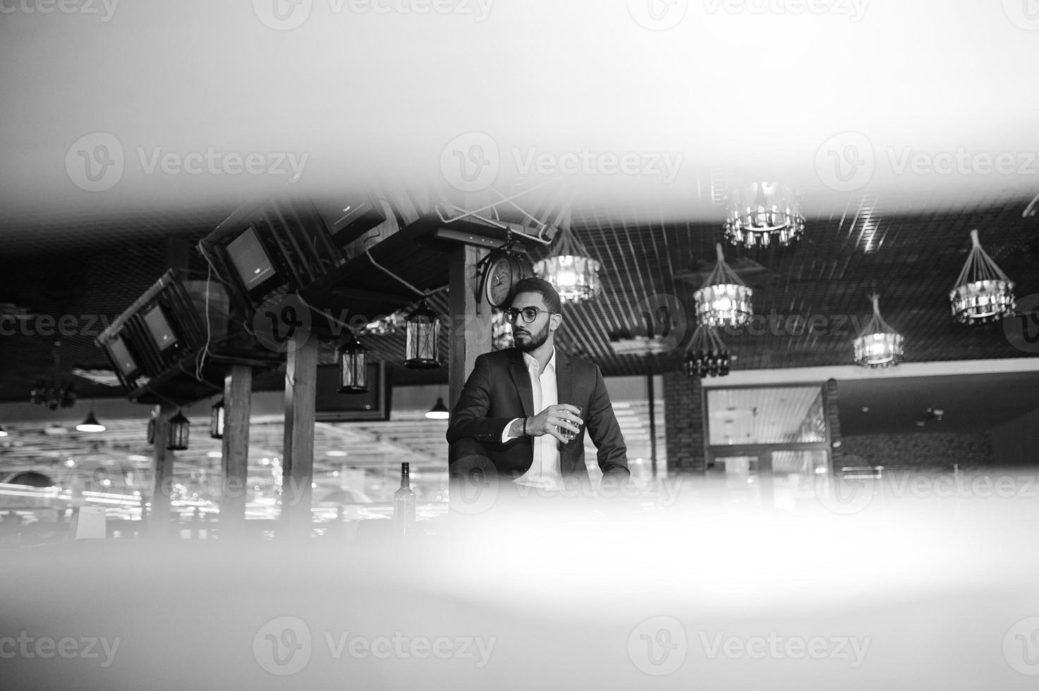 homem árabe bem vestido bonito com copo de uísque e charuto posou no pub. foto