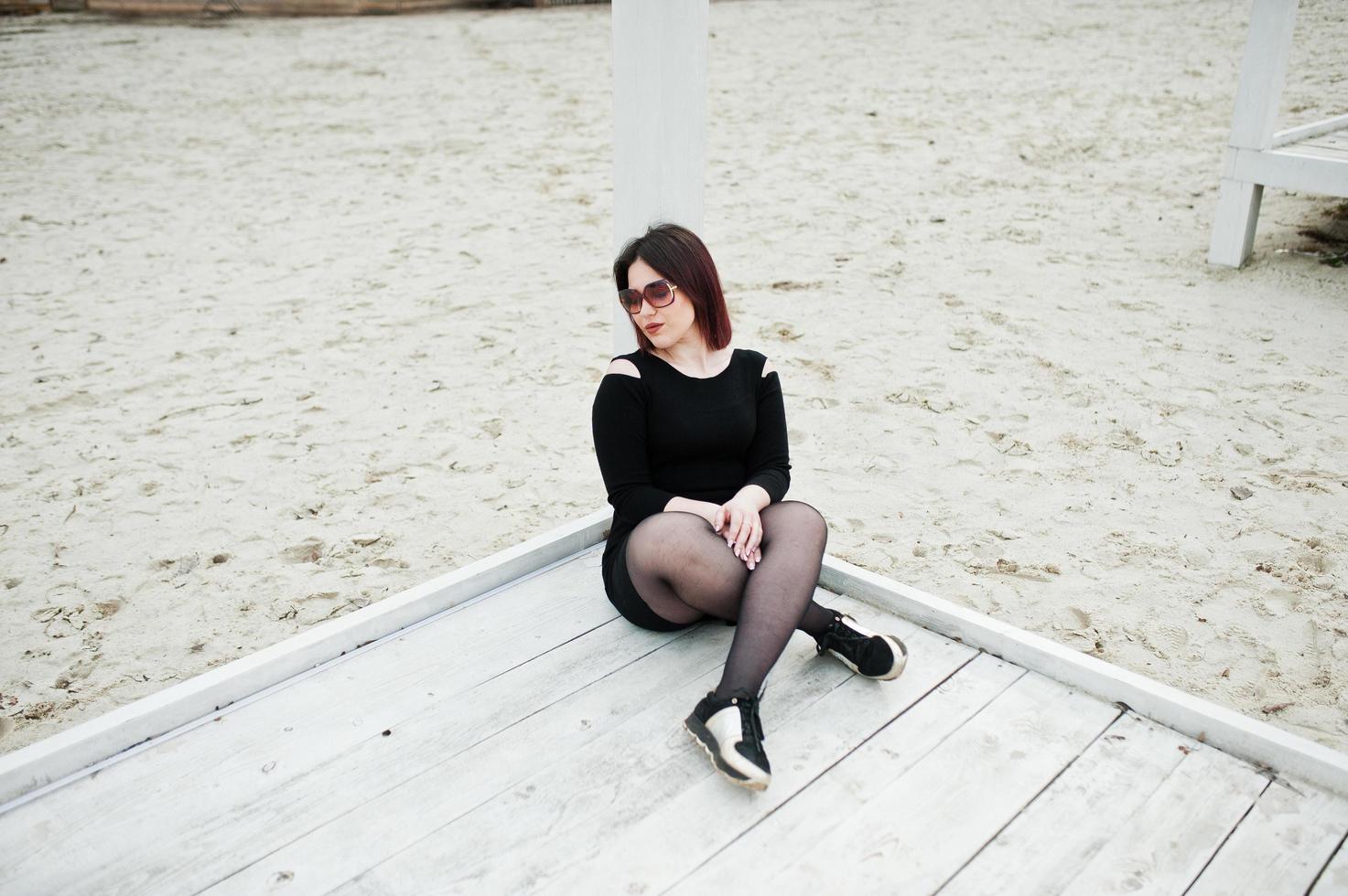 retrato de menina morena de vestido preto, sentado na construção de madeira branca. foto