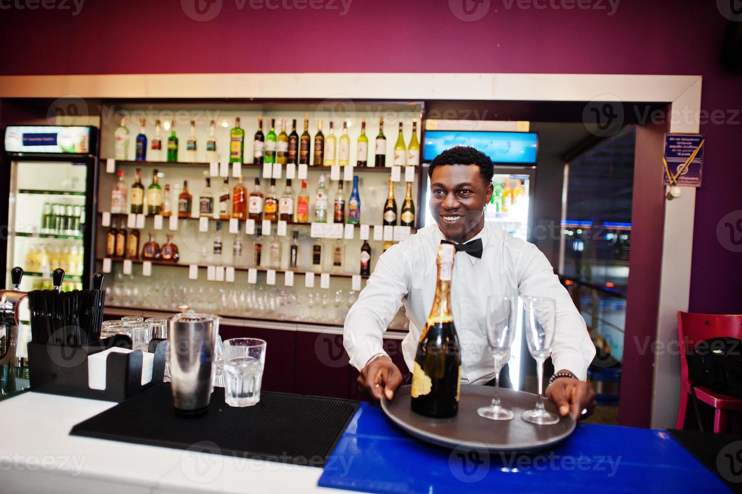 barman americano africano no bar segurando champanhe com copos na bandeja. foto