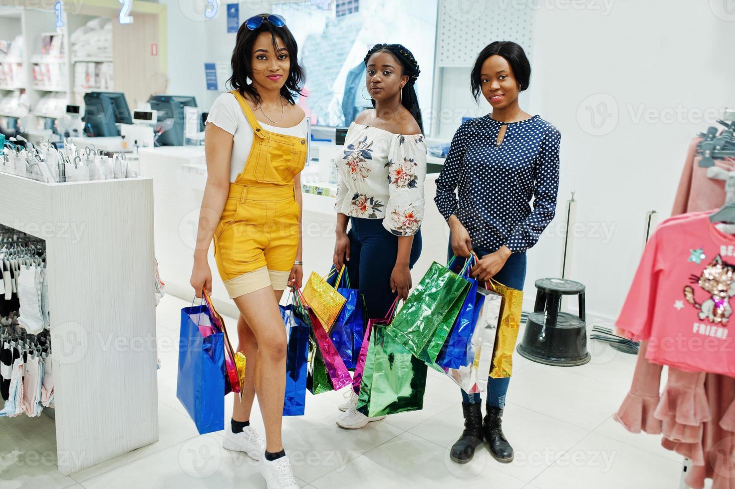 lindas três garotas afro-americanas bem vestidas com sacolas coloridas na loja. foto