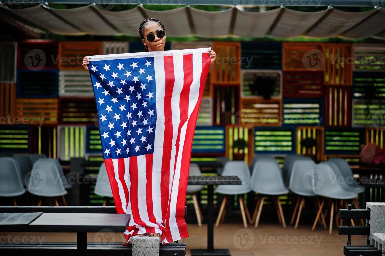 mulher afro-americana elegante em óculos de sol posou ao ar livre com bandeira dos eua. foto