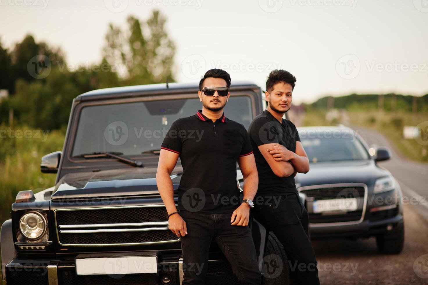 dois irmãos asiáticos vestem todo preto posando perto de carros suv. foto