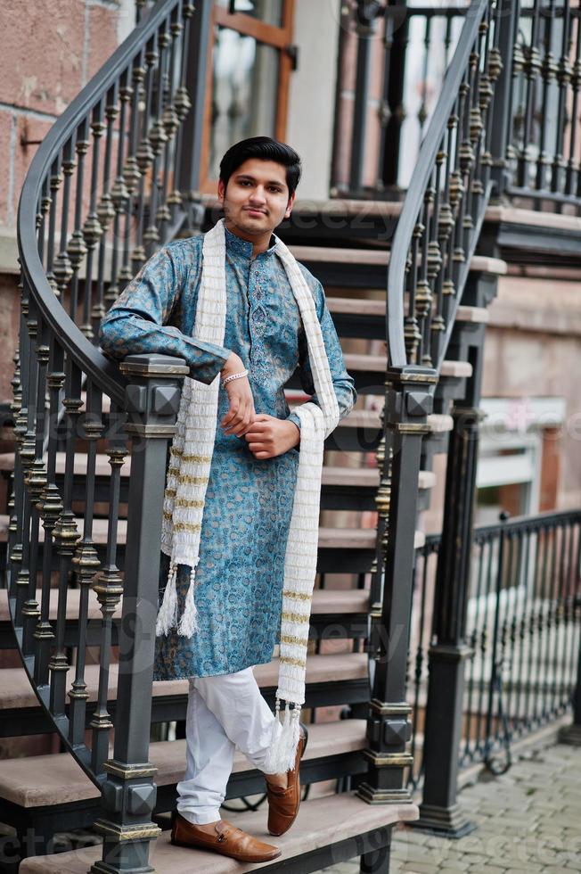 homem indiano usa roupas tradicionais com lenço branco posado ao ar livre contra escadas de ferro. foto