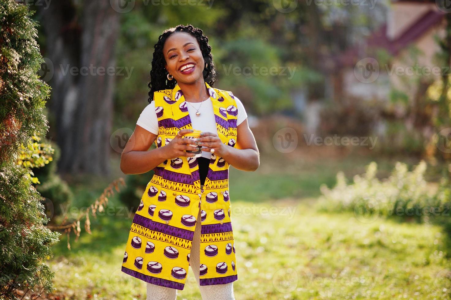 mulheres afro-americanas elegantes na jaqueta amarela posaram na rua com bebida quente em copo de papel descartável. foto