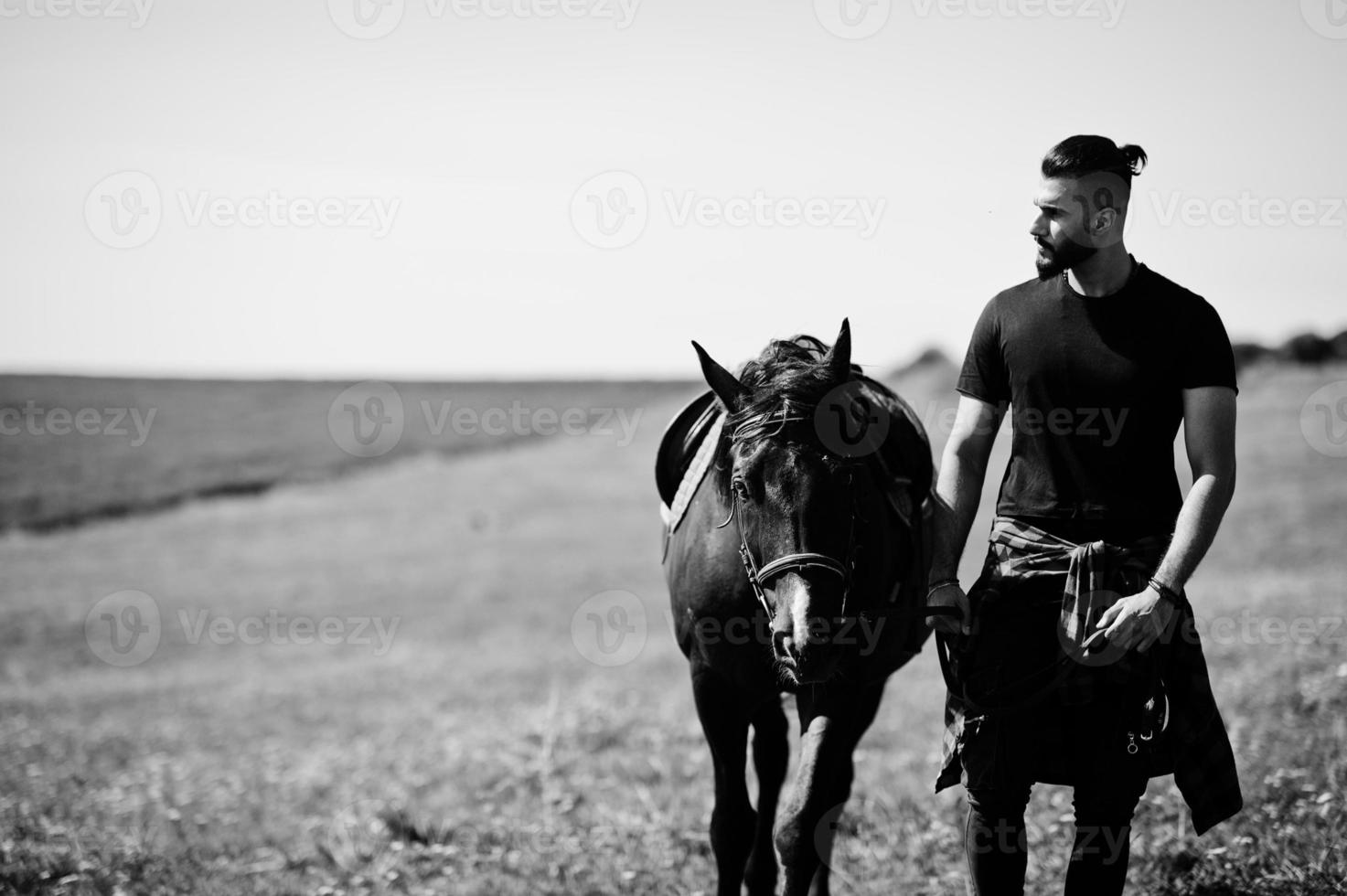 homem árabe de barba alta usa preto com cavalo árabe. foto