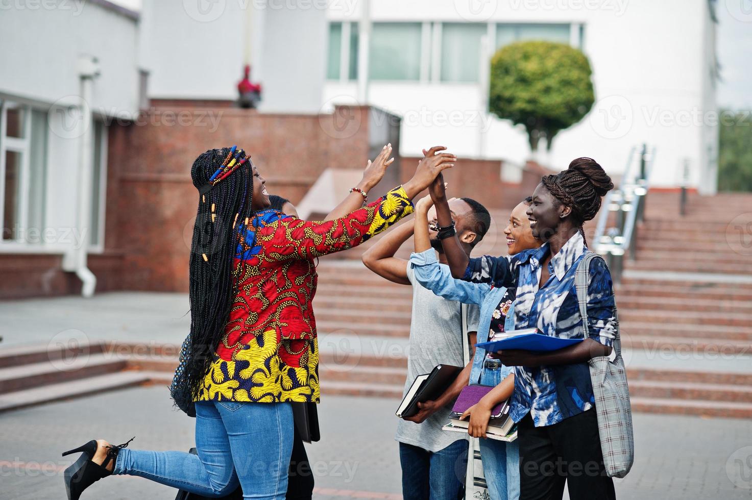 grupo de cinco estudantes universitários africanos passando tempo juntos no campus no pátio da universidade. amigos negros afro estudando e dá mais cinco uns aos outros. foto