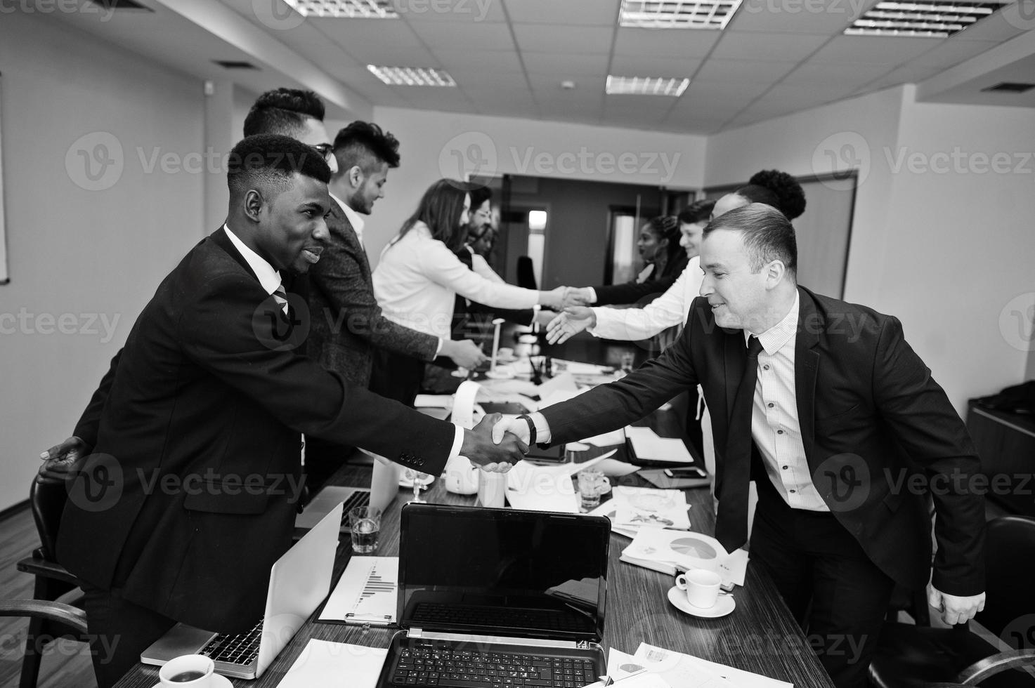 bom negócio. equipe de negócios multirracial abordando a reunião em torno da mesa da diretoria e apertando as mãos um do outro. foto