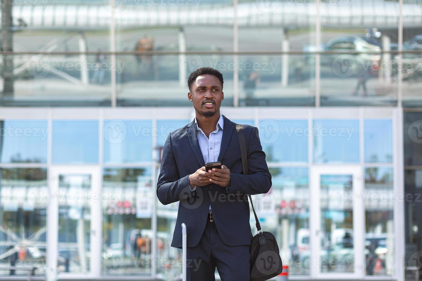 empresário africano viajando perto do aeroporto com mala chamando táxi usando aplicativo móvel foto