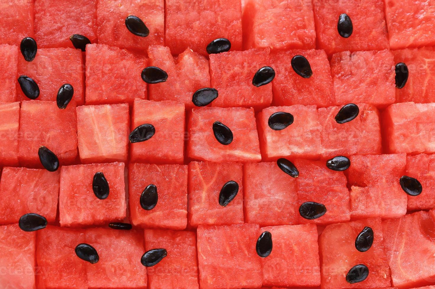 melancia vermelha em cubos disposta em fileiras uniformes, sementes pretas estão espalhadas por cima. pedaços de frutas frescas suculentas dispostas em padrão geométrico de fundo sem emenda. lugar para o seu texto. foto