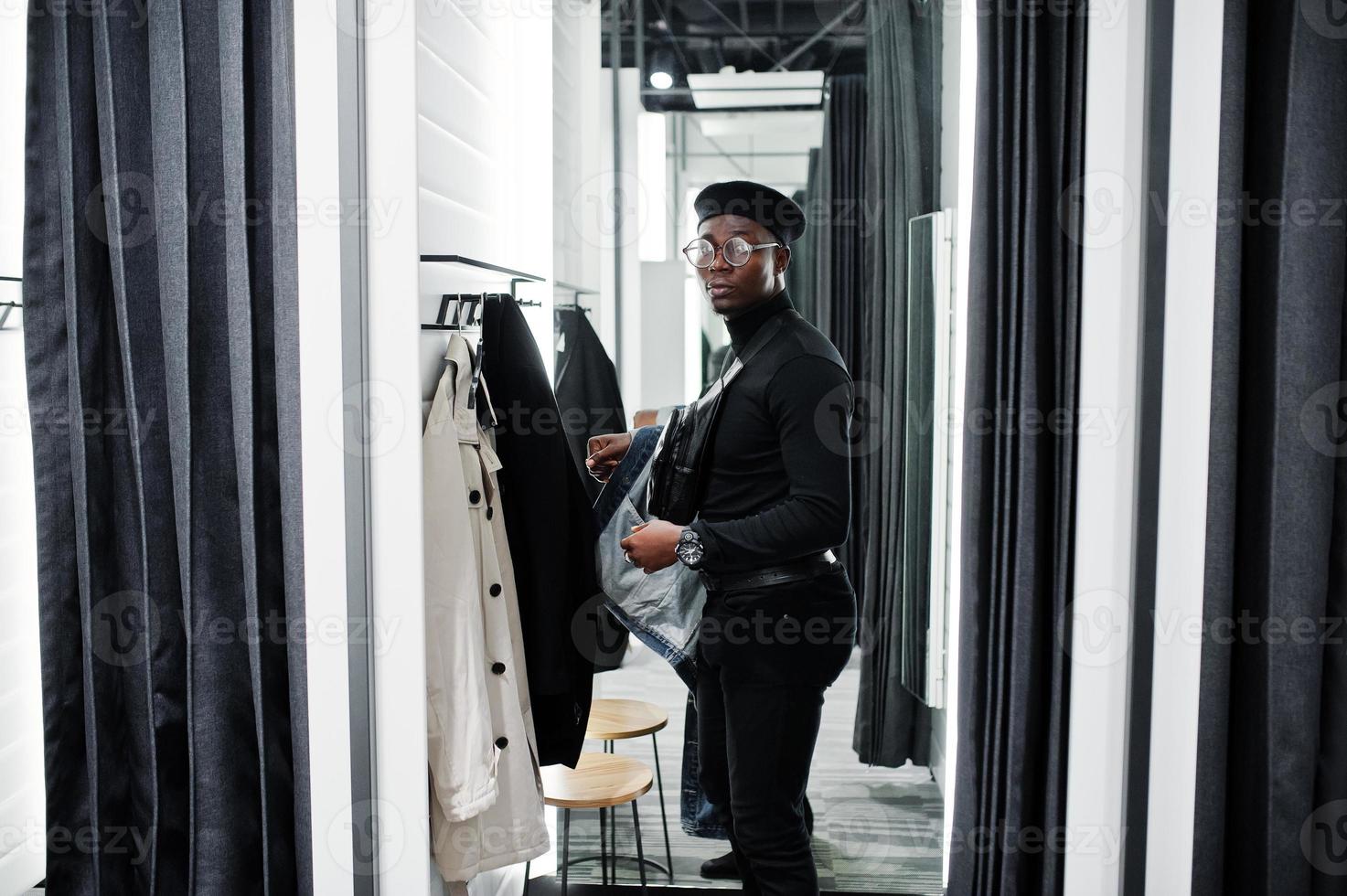 homem afro-americano casual elegante na jaqueta jeans e boina preta na loja de roupas de provador trocar o sobretudo. foto