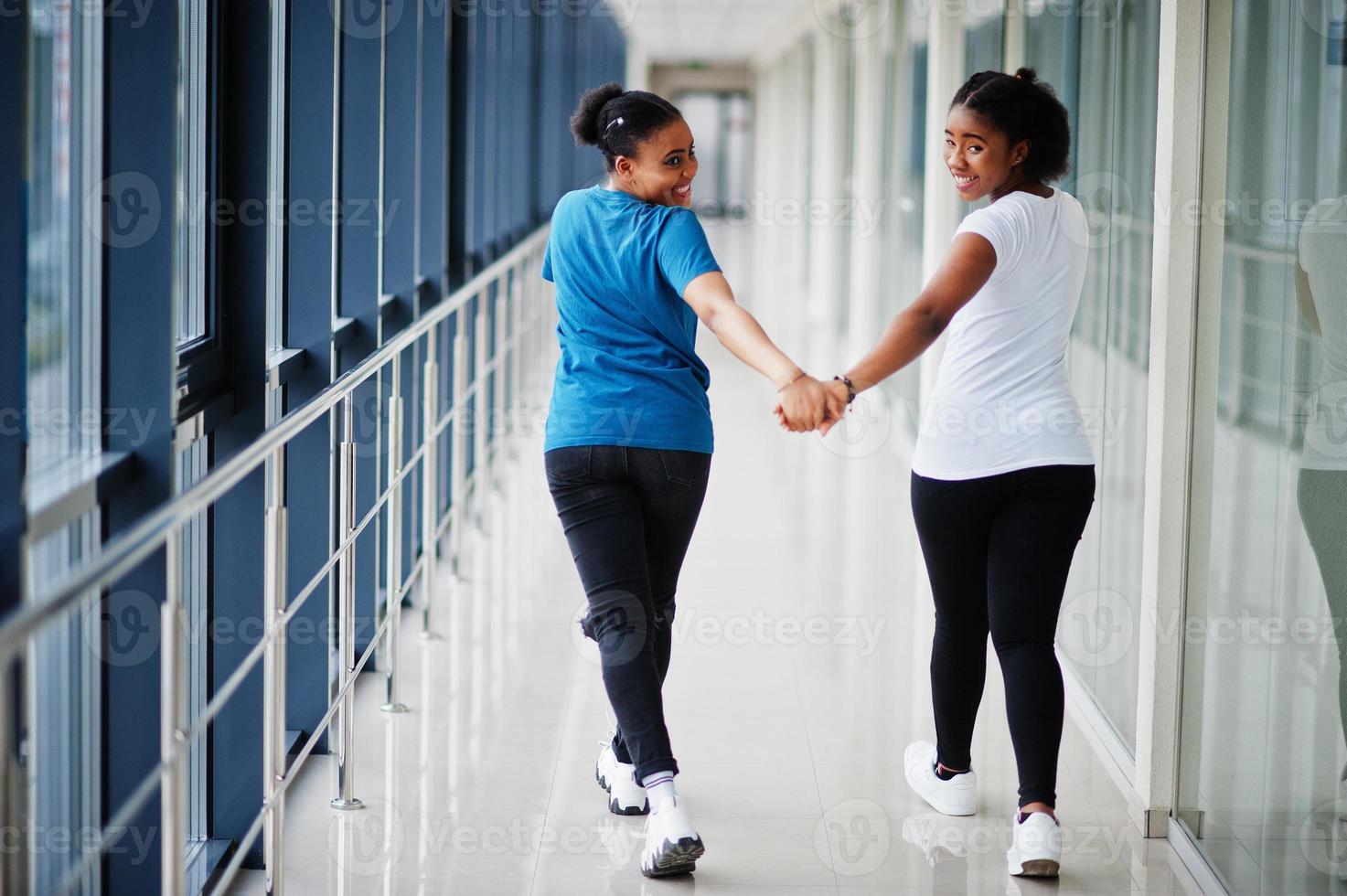 costas de duas amigas africanas em t-shirts andando halding as mãos no interior juntos. foto