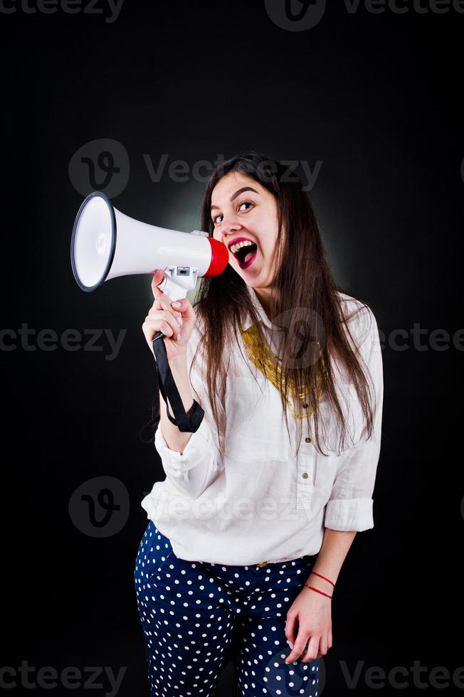 retrato de uma jovem de calça azul e blusa branca posando com megafone no estúdio. foto