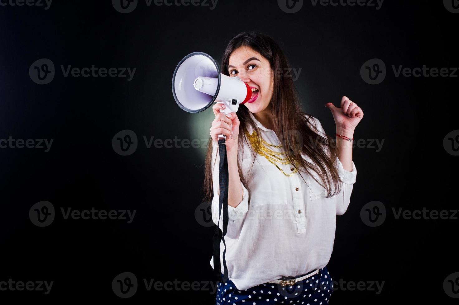 retrato de uma jovem de calça azul e blusa branca posando com megafone no estúdio. foto