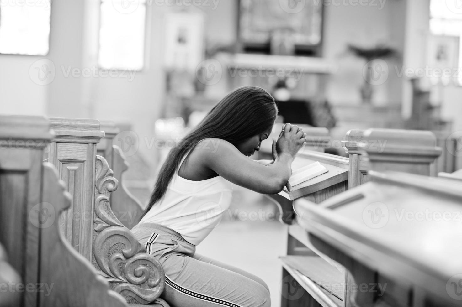 mulher afro-americana rezando na igreja. crentes medita na catedral e tempo espiritual de oração. menina afro cruzou as mãos enquanto está sentado no banco. foto